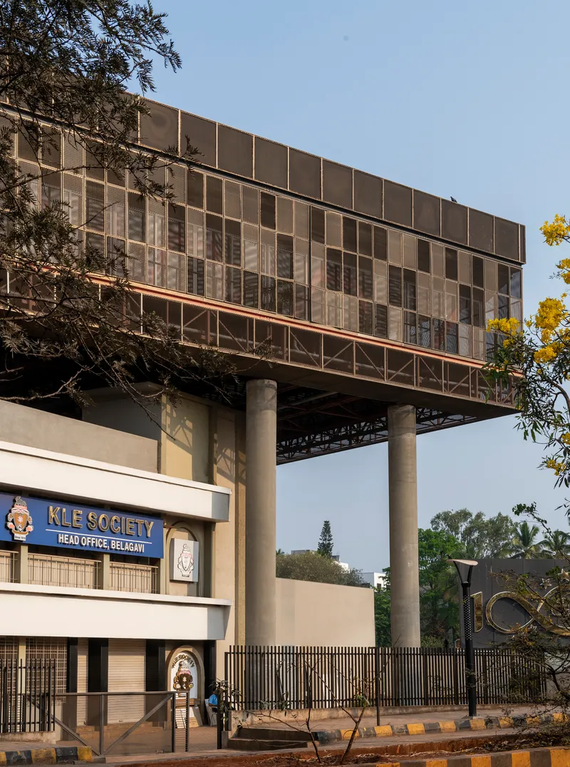 Street view showing the raised glass and panel facade on columns above an institutional entrance gate