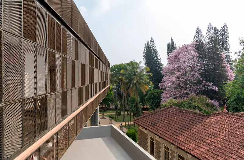 Exterior walkway with perforated metal screen facade overlooking a tiled roof and flowering jacaranda trees