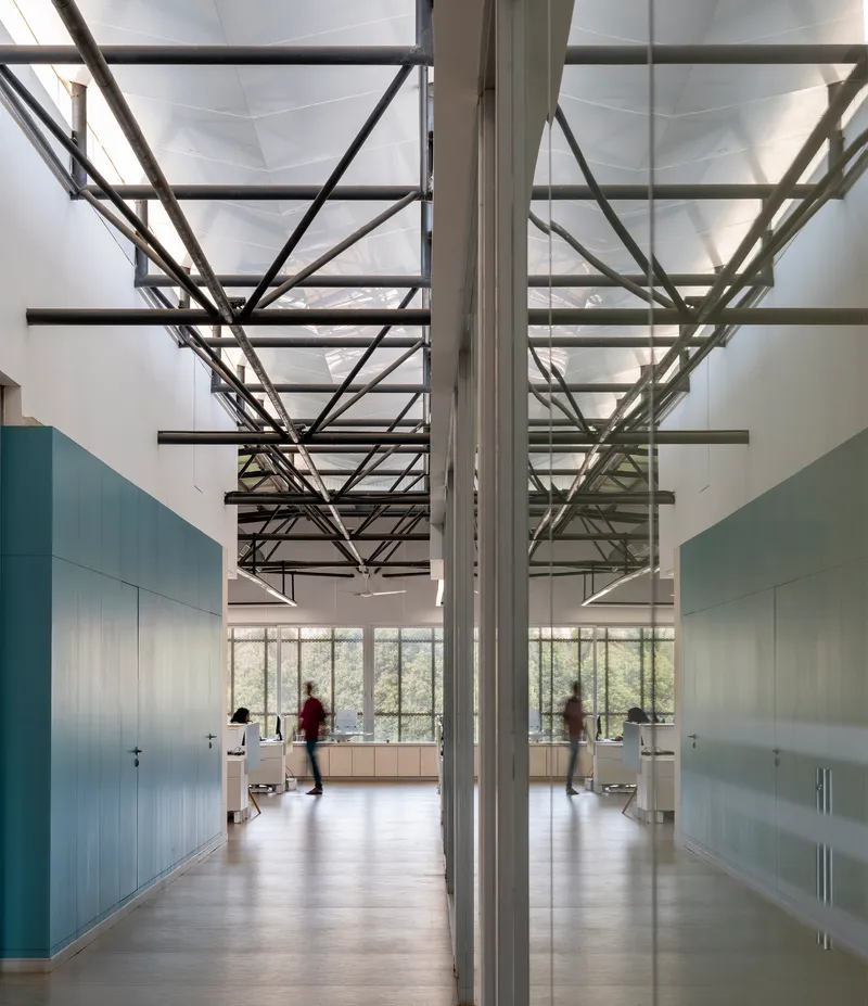 Double-height corridor with exposed steel roof trusses and mirrored wall reflecting people walking through