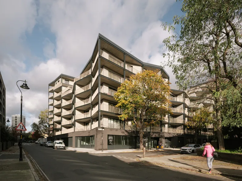 Street corner view of the multi-story residential building with staggered balconies and a yellow tree in autumn
