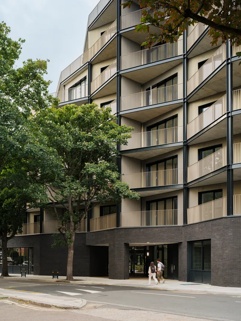 Facade detail showing vertically slatted balcony screens and dark brick base with pedestrians passing by