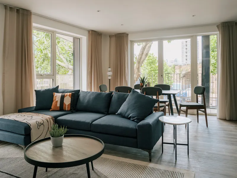 Living and dining area with floor-to-ceiling glazing opening onto a balcony with greenery beyond