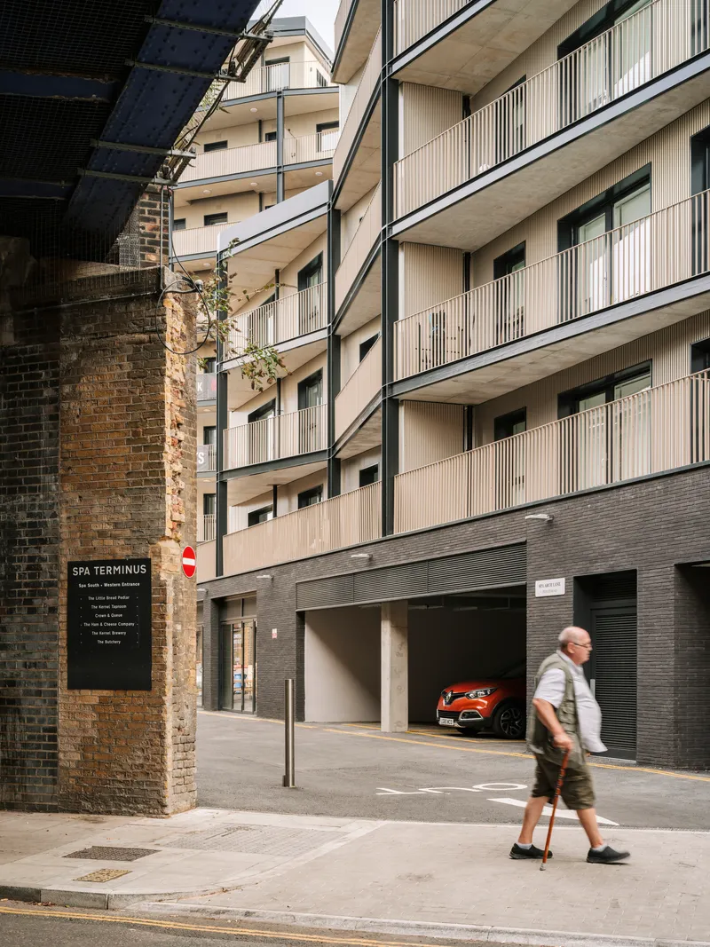Ground-level garage entrance with red car visible and elderly pedestrian walking past brick railway arch