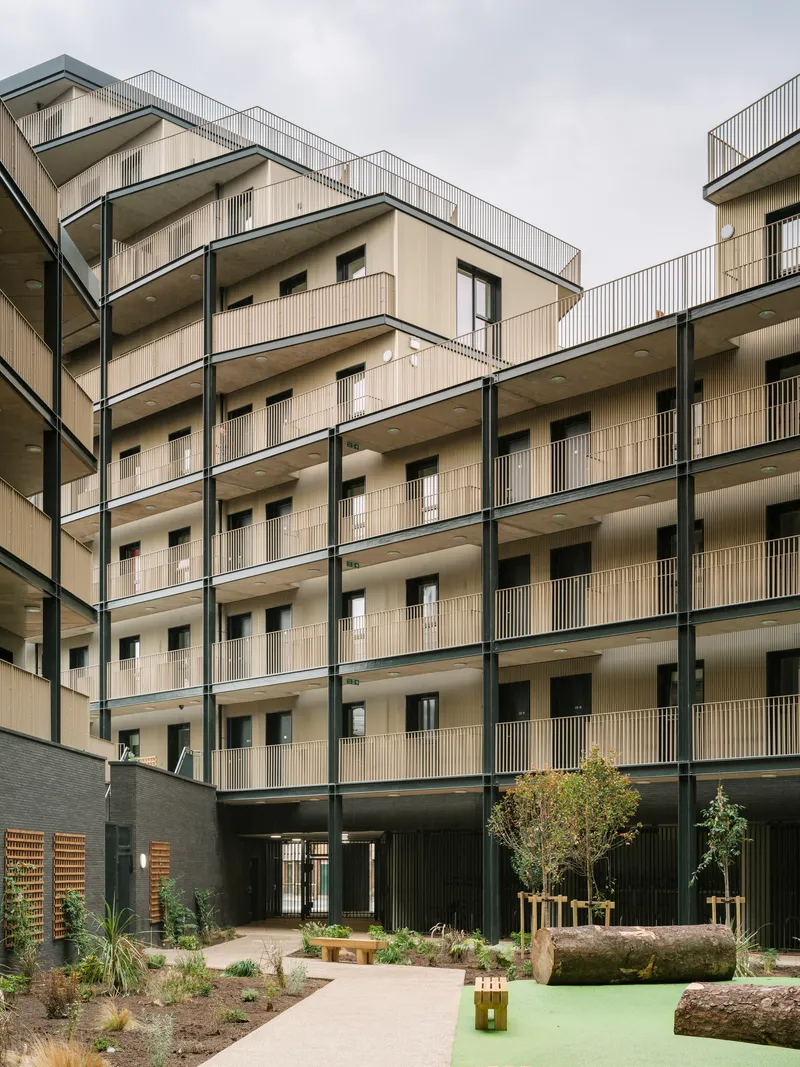 Shared courtyard with planted beds, young trees, and pale facades framing the communal space