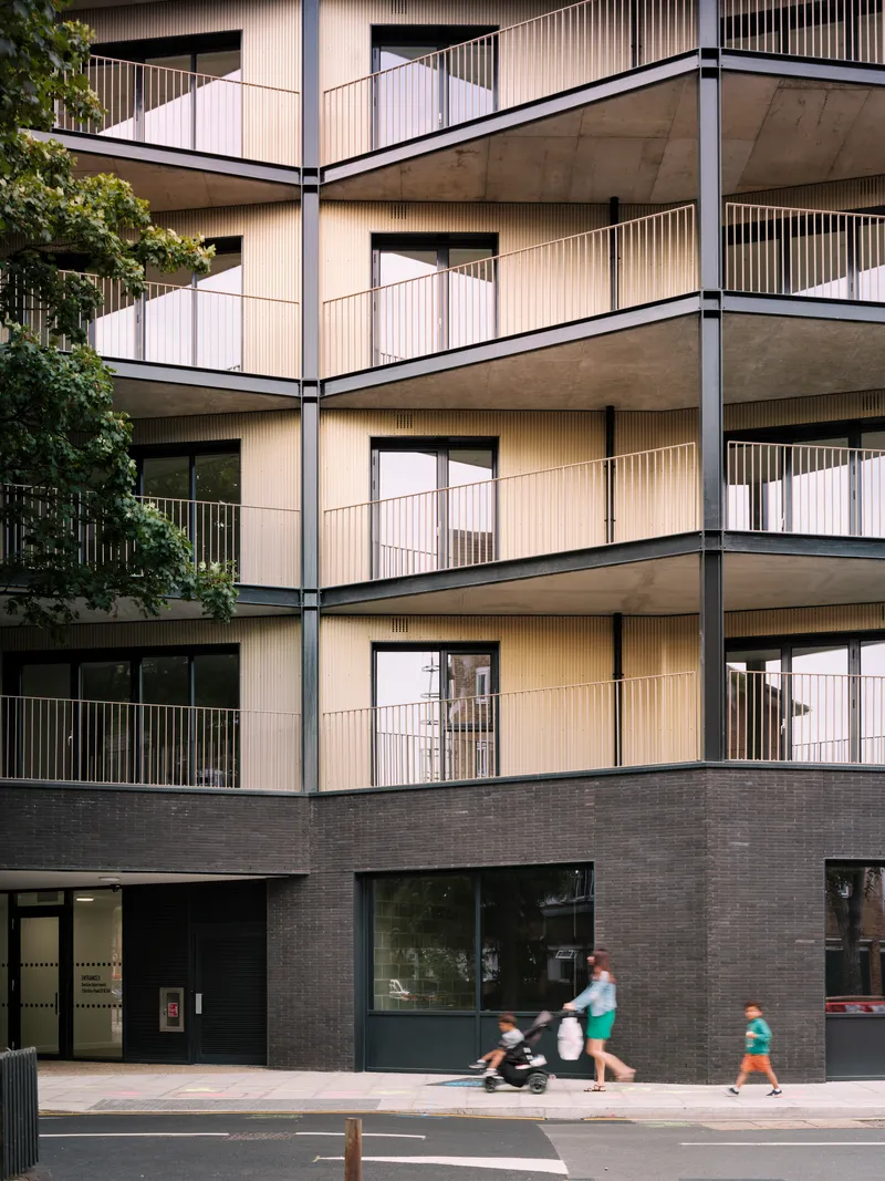 Stacked balconies with vertical metal screening as pedestrians and cyclist move along the pavement below