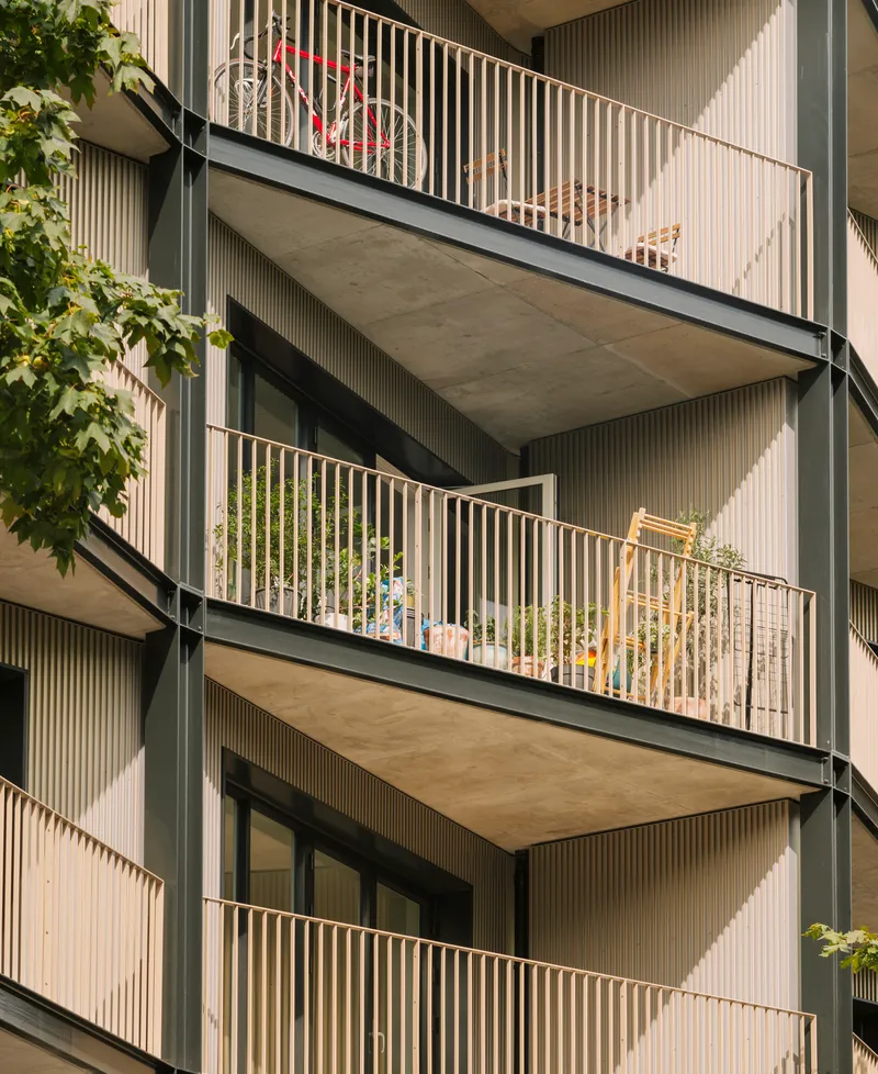 Close-up of stacked balconies with vertical metal railings and concrete soffits framed by tree branches