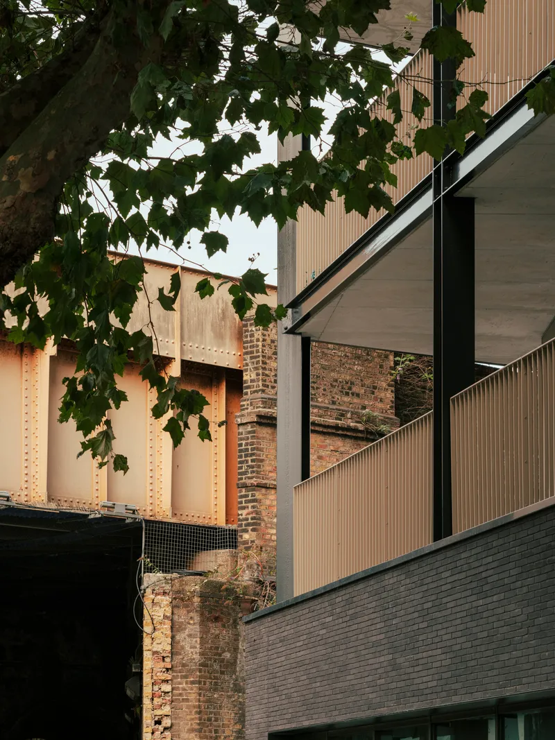 Corner detail where vertical metal cladding meets an adjacent brick wall under dense tree foliage