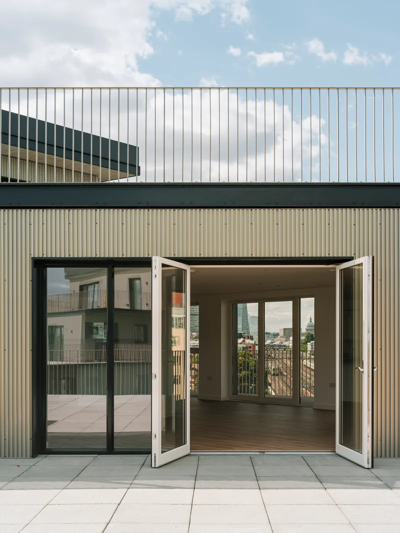 Rooftop terrace with open folding glass doors leading into an apartment under a partly cloudy sky