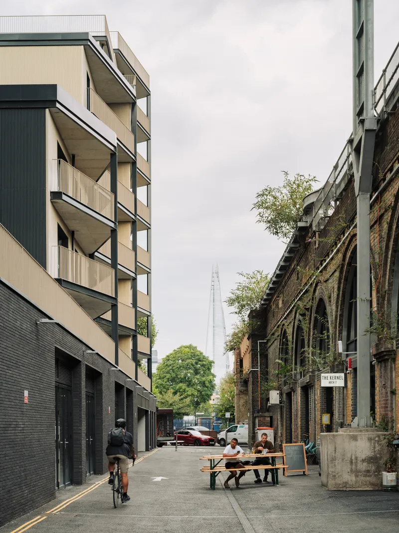 Street view showing the residential facade with alternating balconies and a cyclist passing nearby