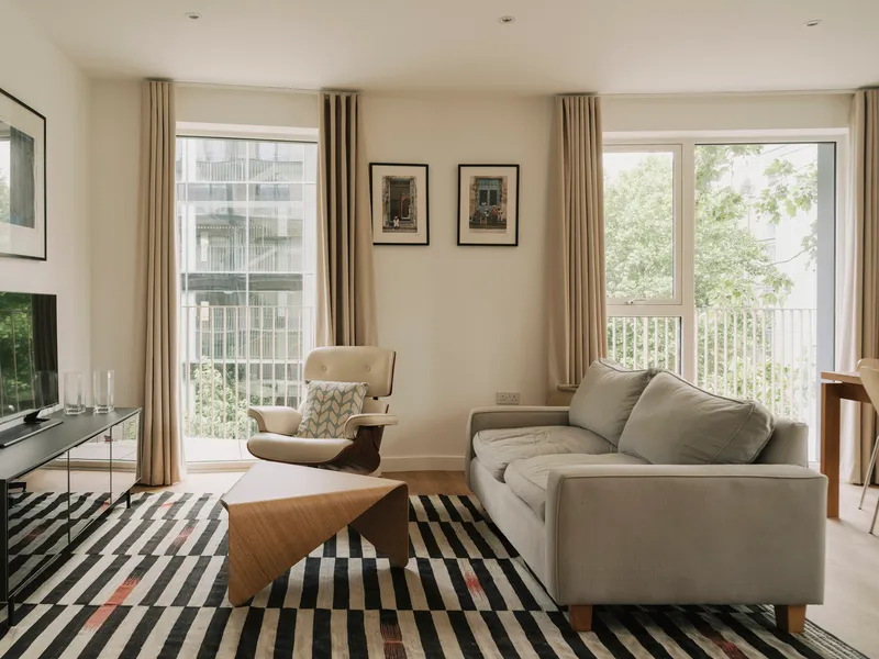 Living room with floor-to-ceiling windows overlooking a balcony with planted beds and neighboring buildings