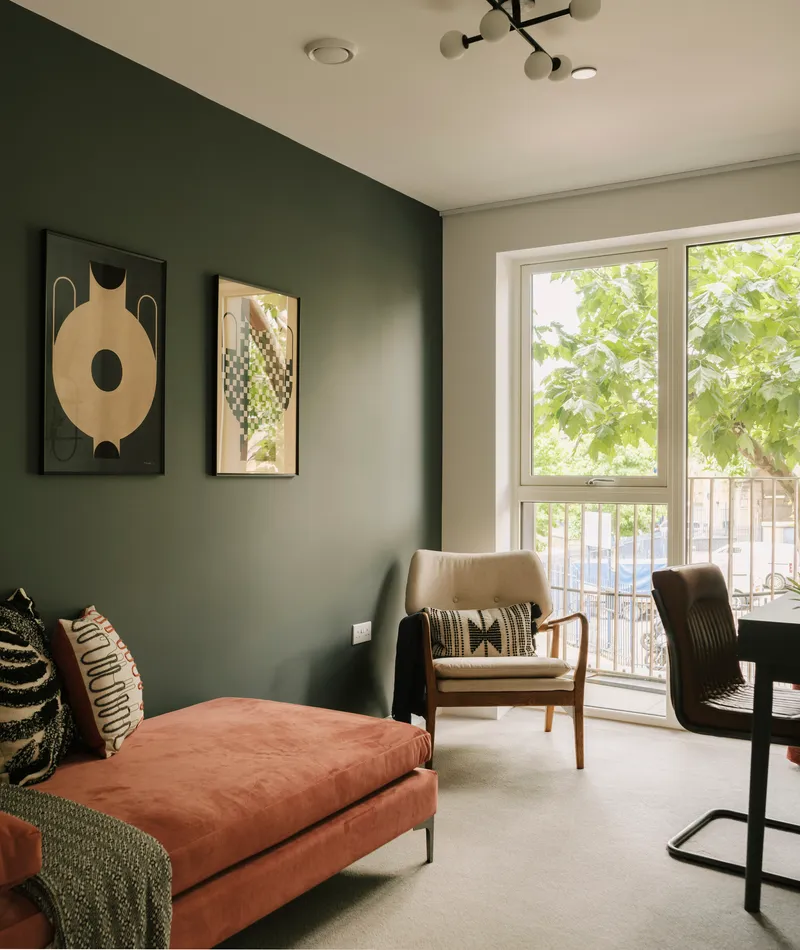 Corner seating area with a green accent wall, framed artwork, and a window with leafy tree views