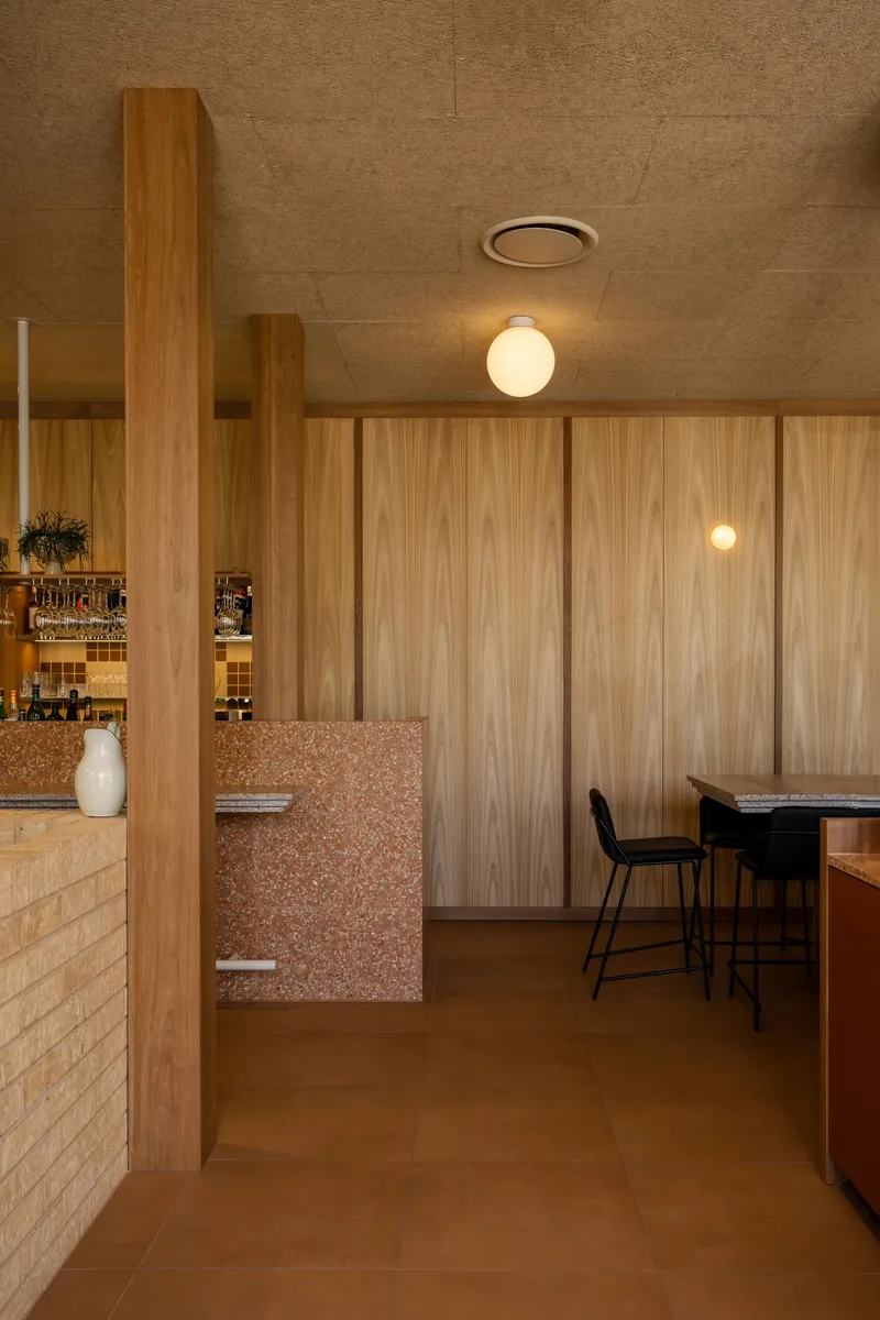 Passageway view toward bar seating with timber columns and terrazzo wall detail