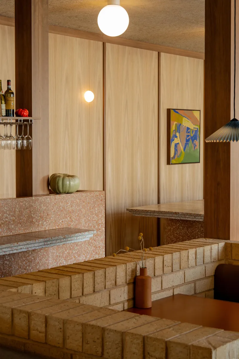 Terrazzo bar counter with integrated seating steps and light timber paneling under warm pendant lighting
