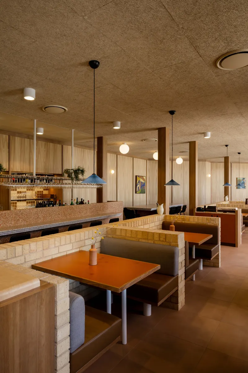 Dining area with booth seating and cream brick dividers under cork ceiling panels and pendant lights