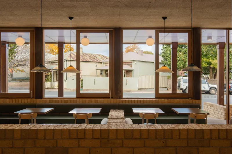 Window wall with timber frames overlooking residential street and autumn trees beyond built-in bench seating