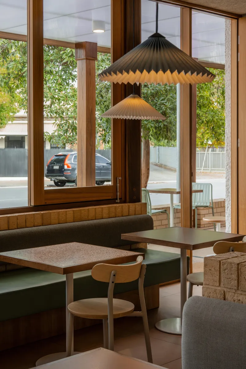 Pleated pendant lamps hanging above booth seating near timber-framed windows facing the street