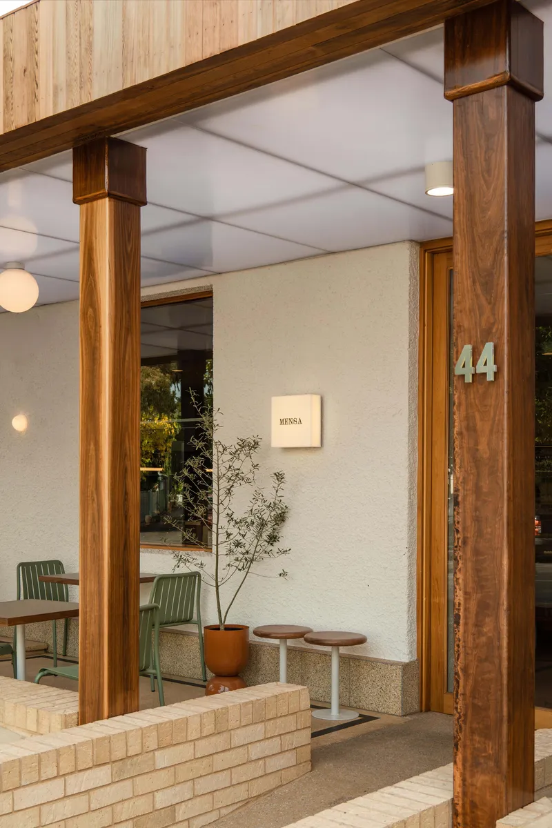 Entrance with timber columns, stucco walls, and a potted plant beside terrazzo flooring