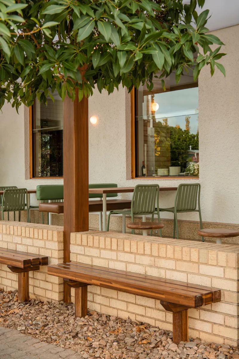Outdoor seating area with cream brick planter wall and timber bench beneath overhanging foliage