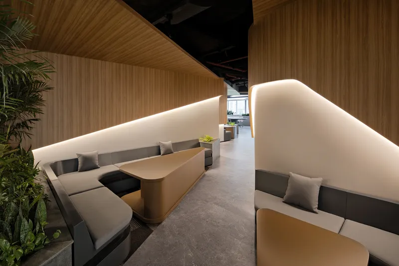 Seating alcove with upholstered benches behind curved backlit white partitions under a timber slatted ceiling