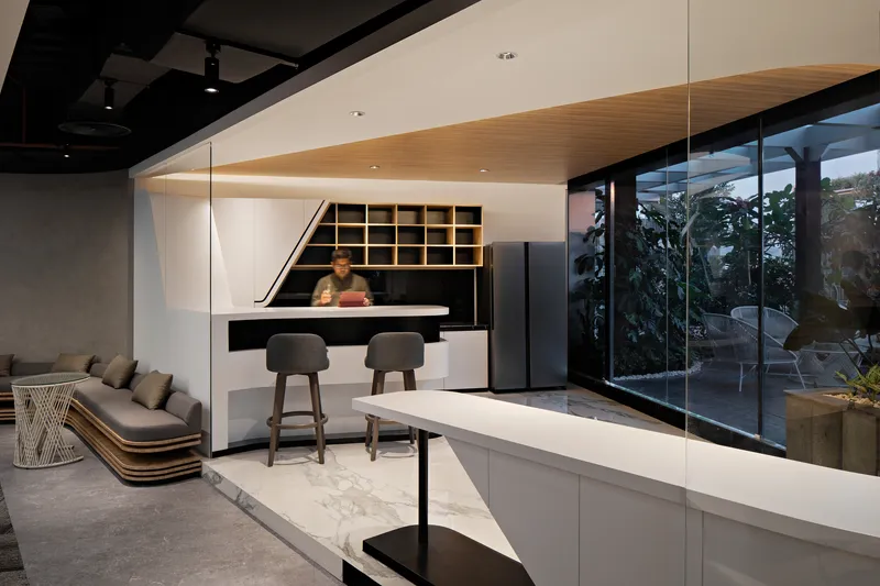 Reception area with timber shelving, black counter, and glass walls opening to tropical greenery