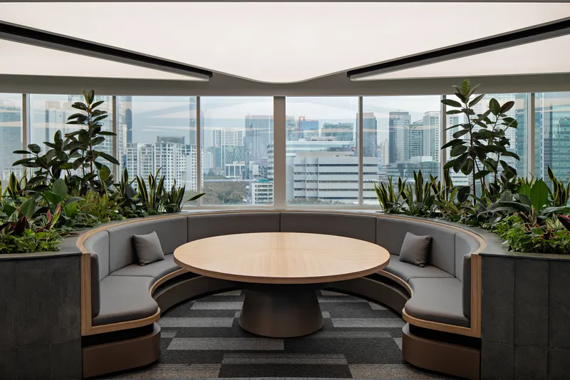 Circular banquette seating around a timber table with integrated planter beds along the curved perimeter