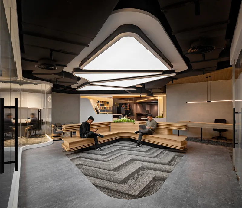 Reception area with tiered timber seating, triangular ceiling light fixtures, and patterned chevron carpet inlay