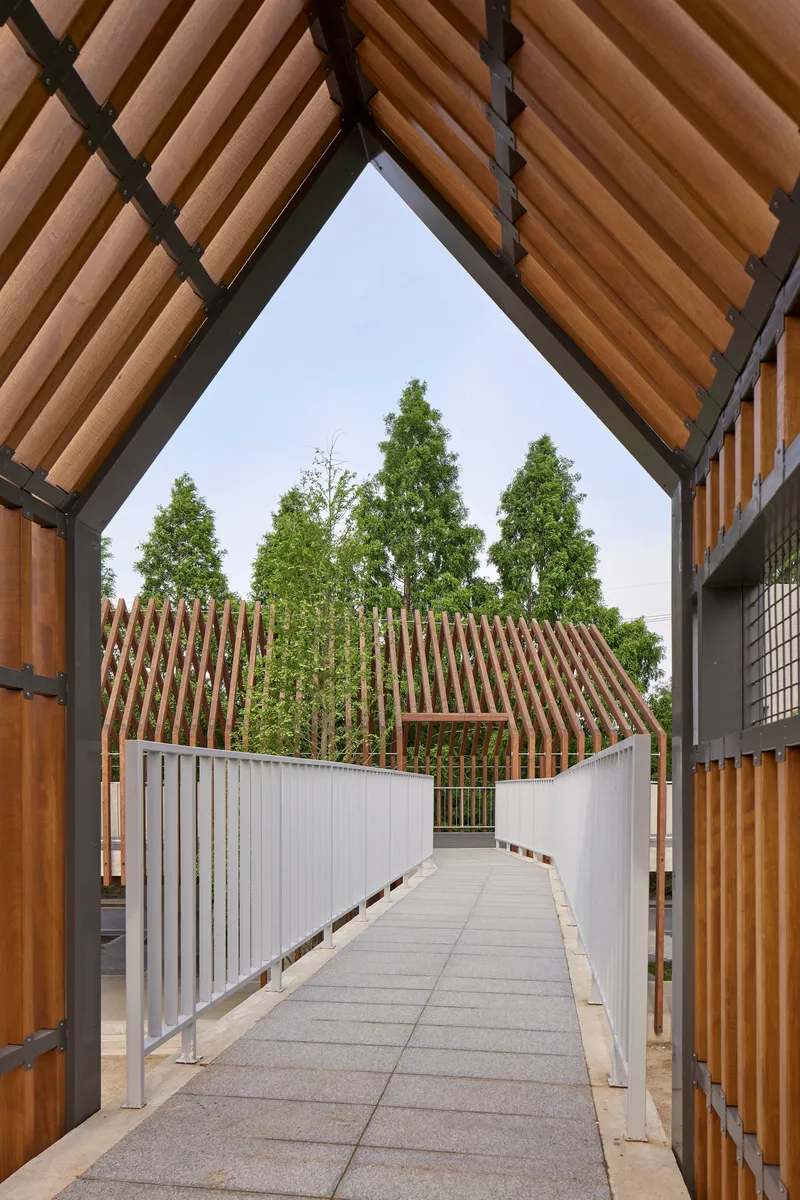 View through timber-framed opening toward the slatted gable structures and connecting bridge