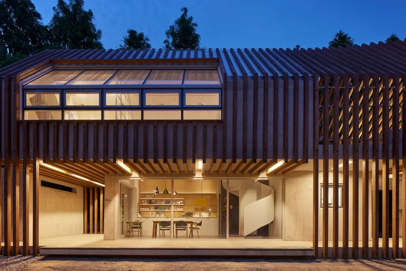 Glass-walled dining area framed by vertical timber louvers and clerestory windows at blue hour