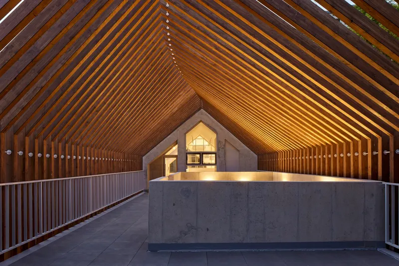 Covered walkway with rhythmic timber slat ceiling and concrete reception desk at twilight
