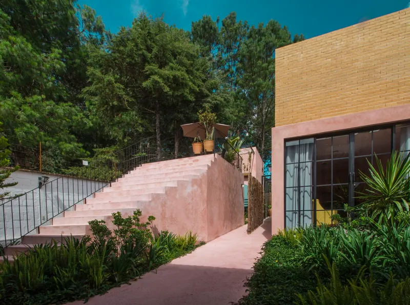 Wide pink stucco staircase ascending between planted beds with yucca and agave under blue sky