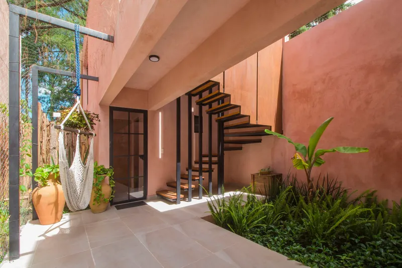 Covered terrace with open-tread steel staircase, potted plants and dappled midday sunlight