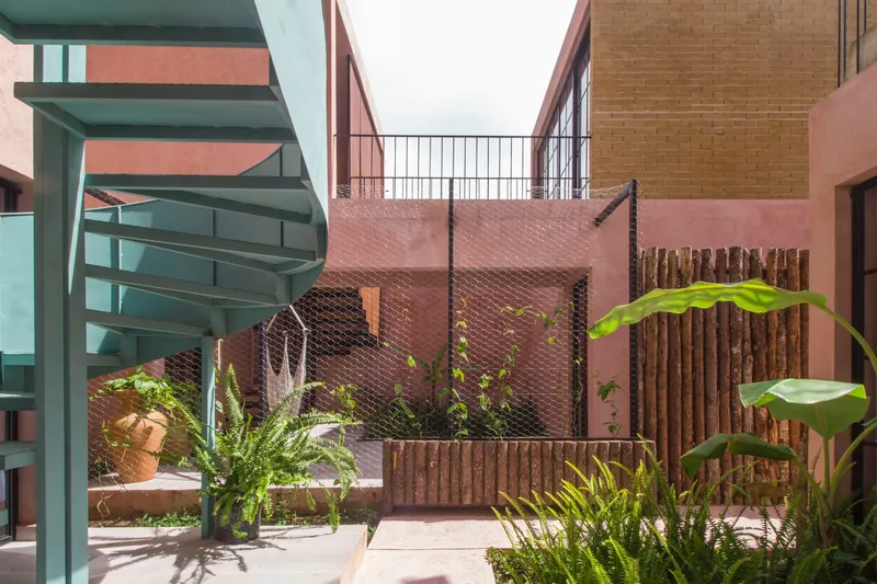 Courtyard with pink textured walls, vertical timber screening, and potted tropical plants beneath an overcast sky
