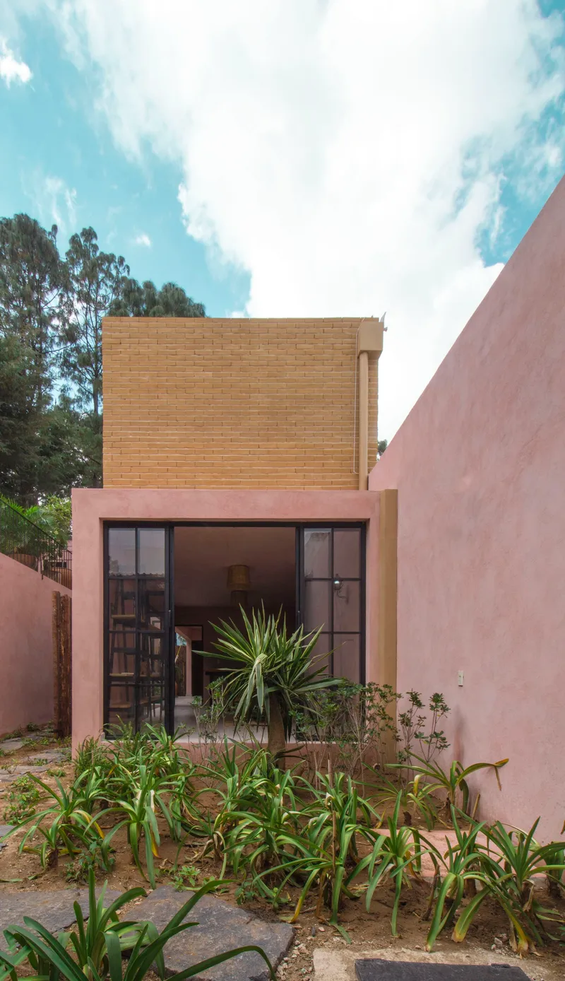 Garden facade with black-framed glazed door beneath a tan brick volume and lush planted bed