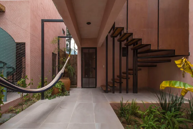 Tiled passageway with steel-framed staircase, hammock, and tropical plants against pink stucco walls
