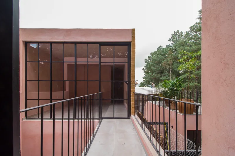 Upper-level terrace with metal railing leading to a gridded glazed wall facing surrounding trees
