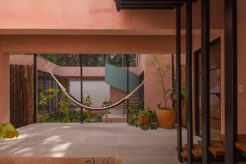 Interior view through steel-framed glazing to courtyard with hammock, spiral stair, and potted plants