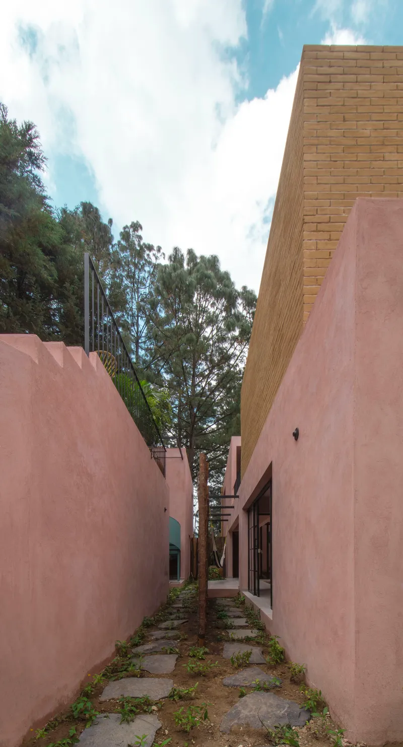 Narrow outdoor passage between pink stucco walls with stone pavers and tan brick volume above