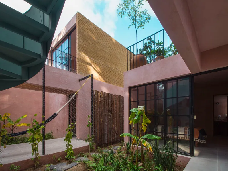 Courtyard view showing pink stucco walls, bamboo screening, glass doors, and planted beds under blue sky