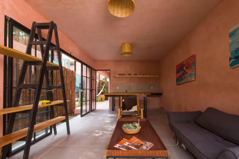 Interior living space with steel-framed glazing, ladder shelving, woven pendant lights, and pink stucco walls
