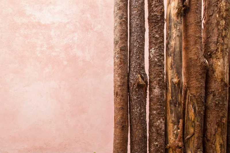 Detail of vertical bamboo poles meeting pink stucco wall at weathered junction