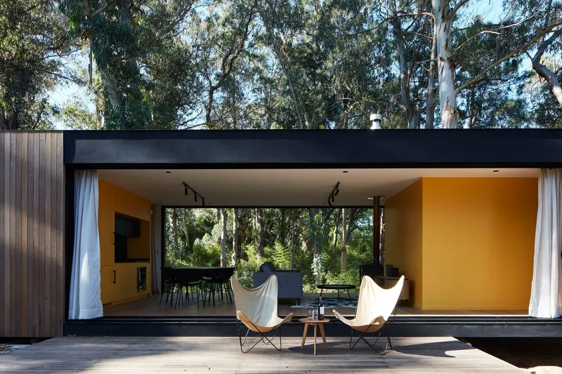 Covered terrace with butterfly chairs on timber decking beneath a flat black soffit looking into the living space