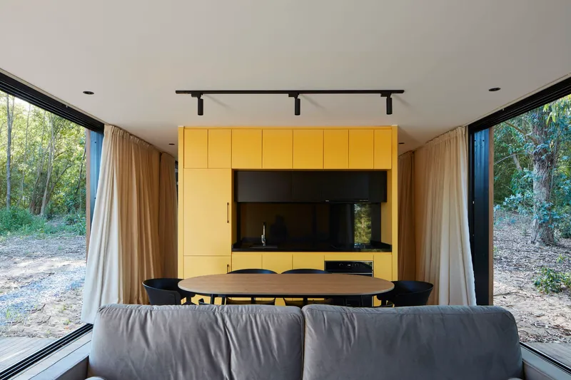 Interior view of the dining area with yellow cabinetry and full-height glazing opening to the forest