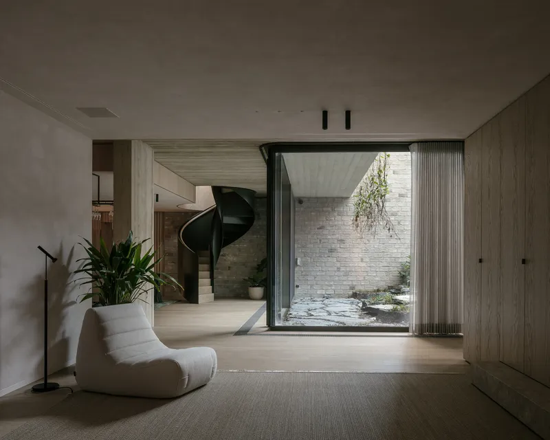 Interior room with light timber flooring opening to a small courtyard with brick walls and hanging greenery