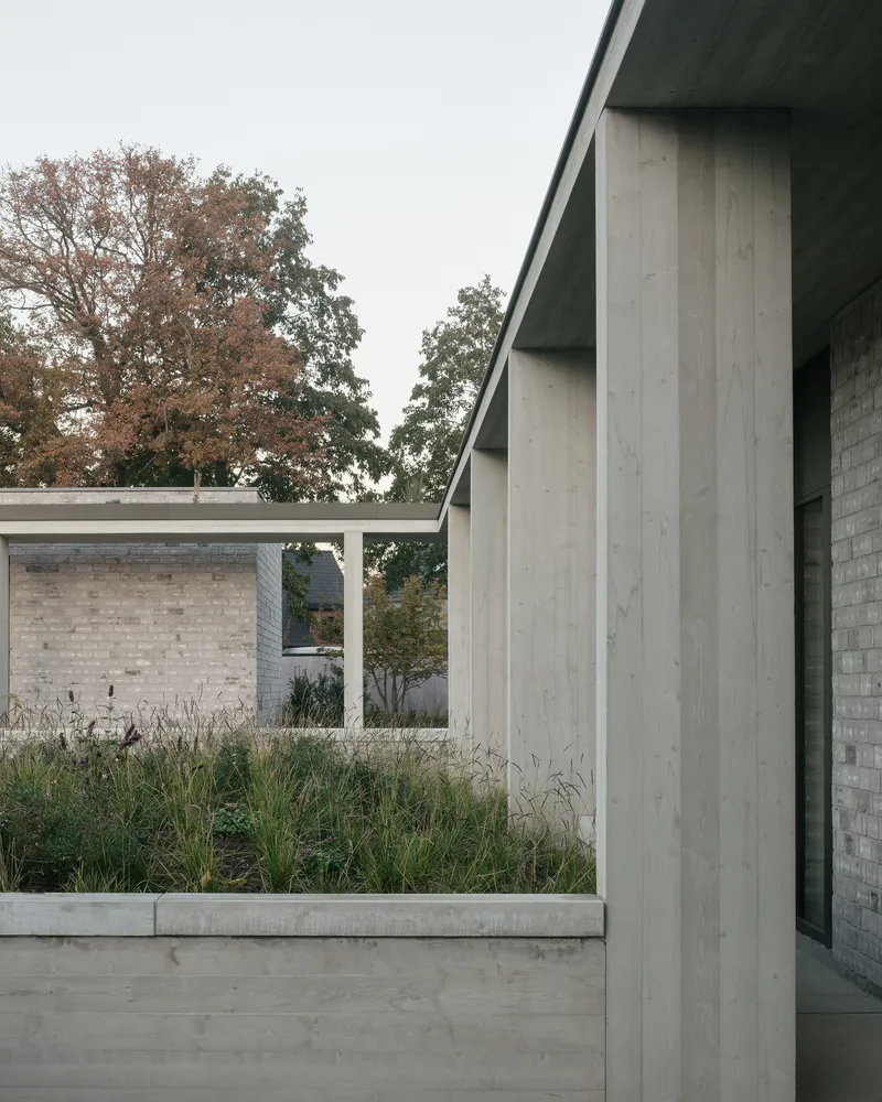Concrete columns framing a planted bed with ornamental grasses beneath an autumn canopy