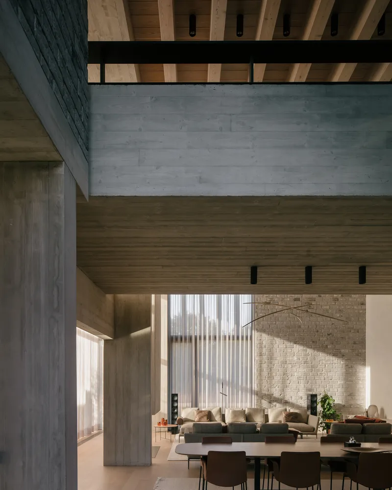 Double-height living space with exposed timber ceiling beams and concrete columns in afternoon light