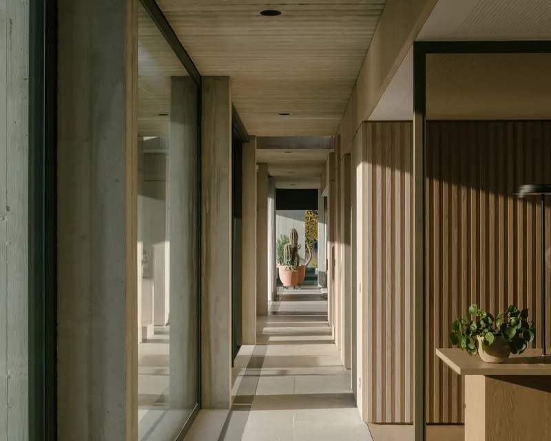Corridor with vertical timber slat screens and glazed walls looking onto planted courtyards