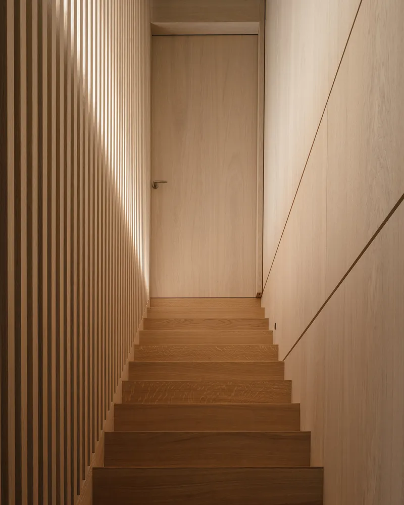 Timber staircase ascending between vertical slat wall and angled paneled surface