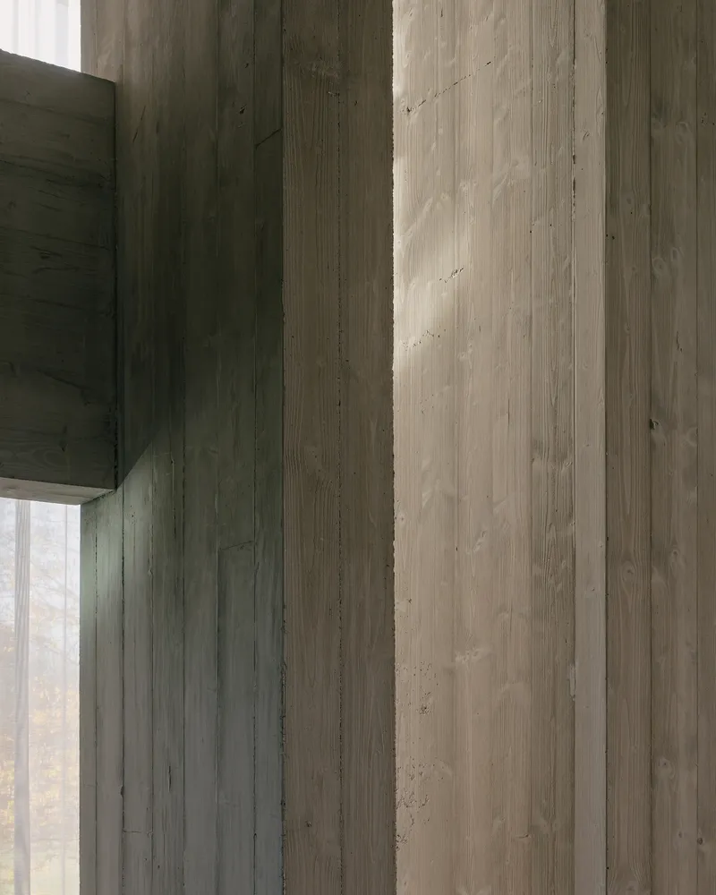 Board-formed concrete wall and beam junction with vertical formwork texture visible in natural light