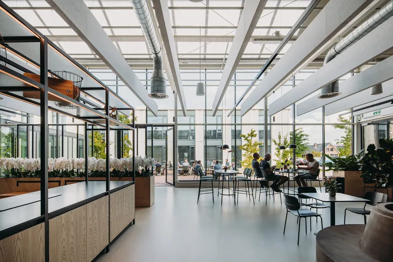 Interior cafeteria with gridded skylight structure, exposed ducts, and people seated at tables