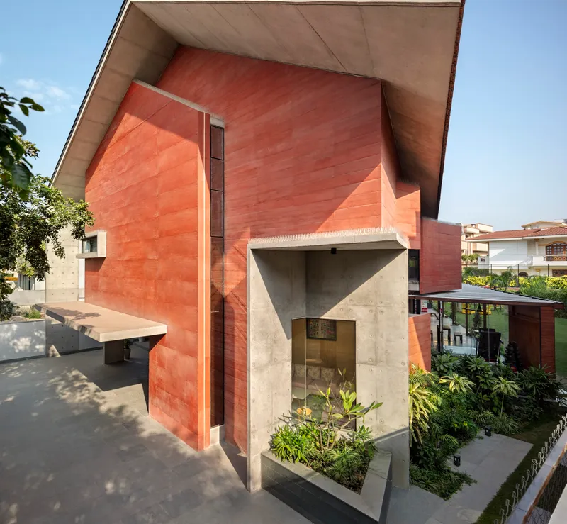 Red sandstone volumes with a concrete entry portal and planted courtyard below in afternoon light